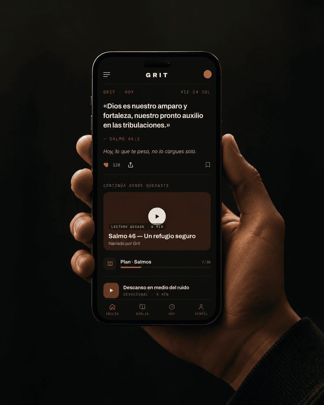 Una mano sostiene un teléfono con la pantalla de inicio de Grit abierta, mostrando el versículo del día.